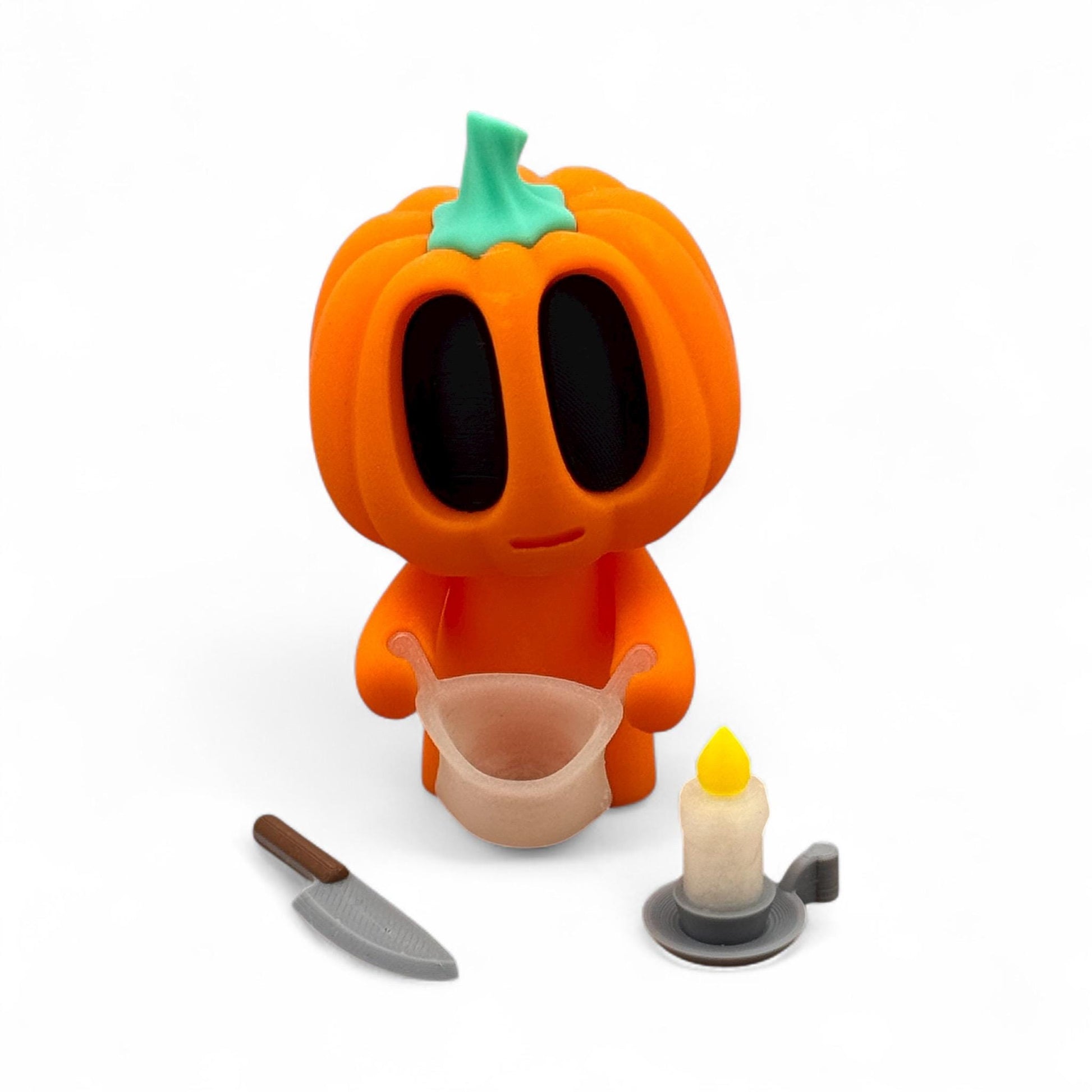 Blob Pumpkin Figur als Halloween-Deko, orangefarbener Kürbis mit schwarzem Gesicht, hält einen Beutel in den Händen, daneben Messer und Kerze, 3D-gedruckt.