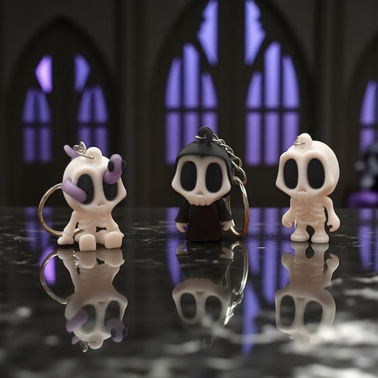 Drei 3D-gedruckte Schlüsselanhänger: Skelett-Blob (weiß/lila), Grim-Reaper in Robe und Skelett-Blob (weiß) mit Schlüsselring auf dunklem Tisch – Halloween Produktfoto.
